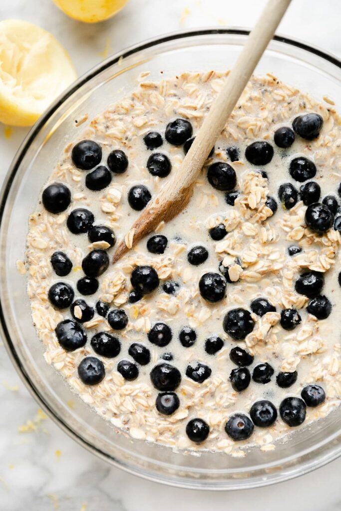 Close up bowl of lemon blueberry baked oatmeal ingredients being stirred with a wooden spoon.