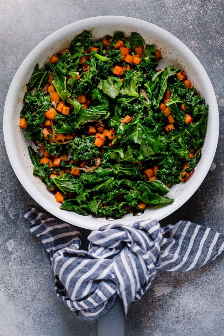 Bright green Kale and orange sweet Potato Saute in a white bowl. 