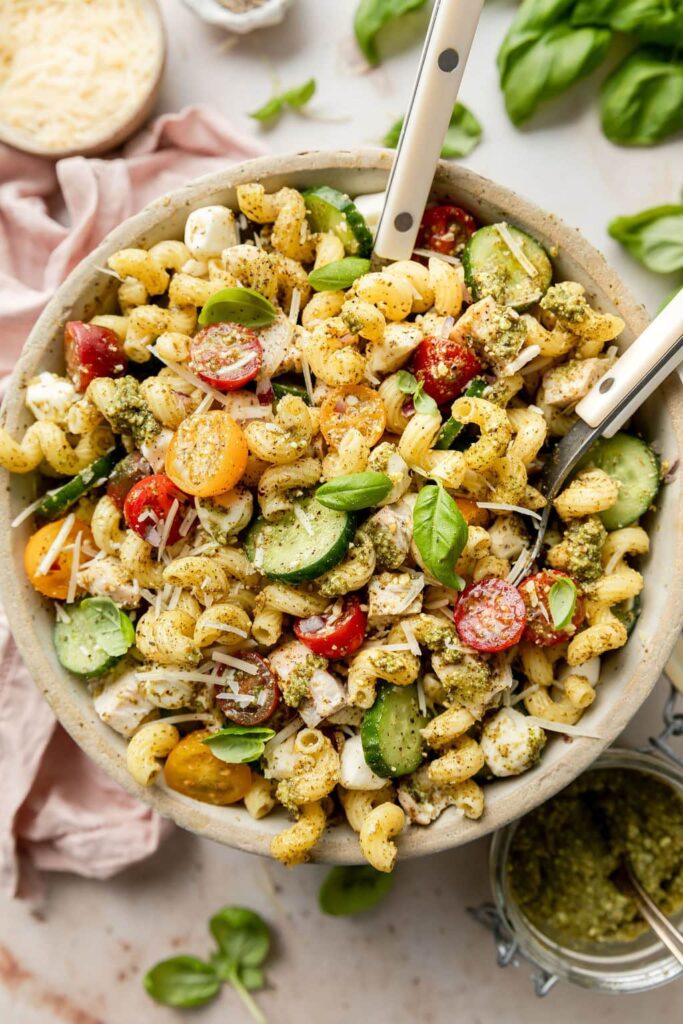 Overhead view stone bowl filled with chicken pesto pasta salad topped with fresh Parmesan cheese shreds