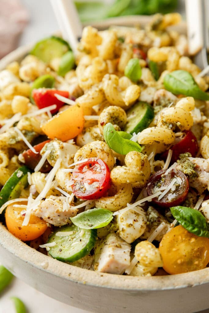 Close up view pesto pasta salad with cucumbers, tomatoes and fresh basil and Parmesan cheese