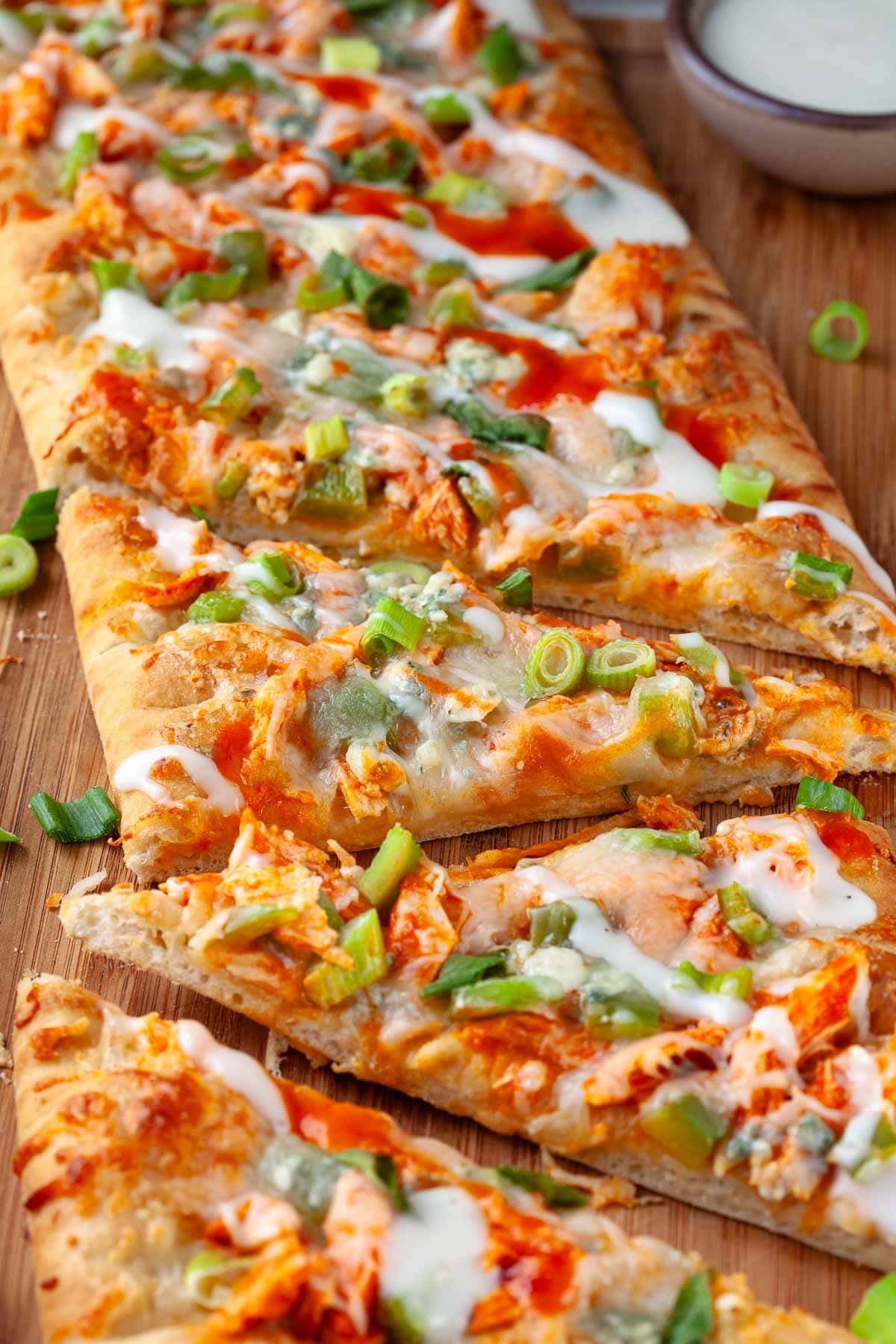 close up of buffalo chicken flatbread slices with green onion garnish on wood cutting board