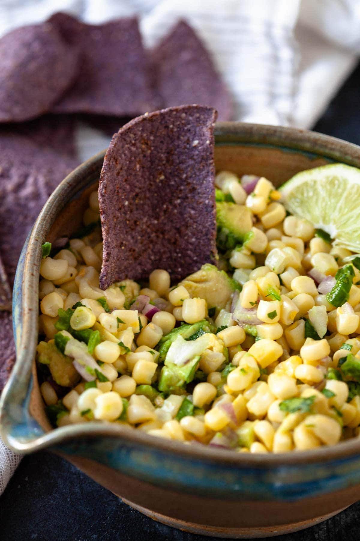 corn salsa with avocado, red onion, cilantro with lime wedge and blue tortilla chip in brown and blue bowl