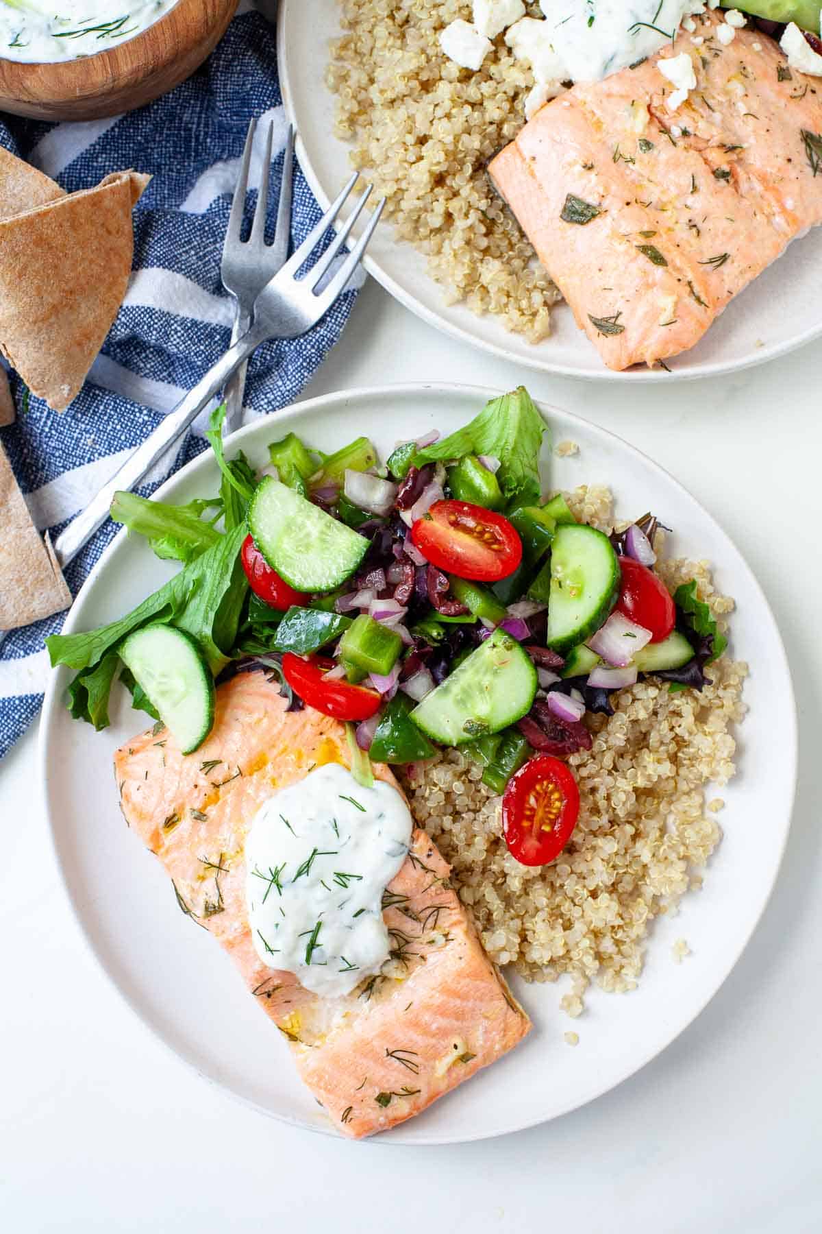 bowl with salmon, quinoa, cucumber, tomato, onion, bell pepper, and olives covered in tzatziki
