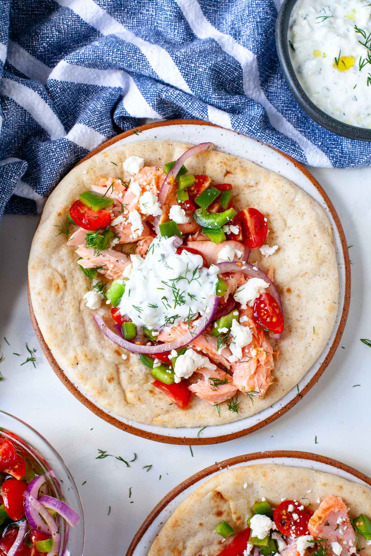 flaked salmon with tomatoes, bell pepper, tomatoes, red onion and tzatziki on top of pita bread